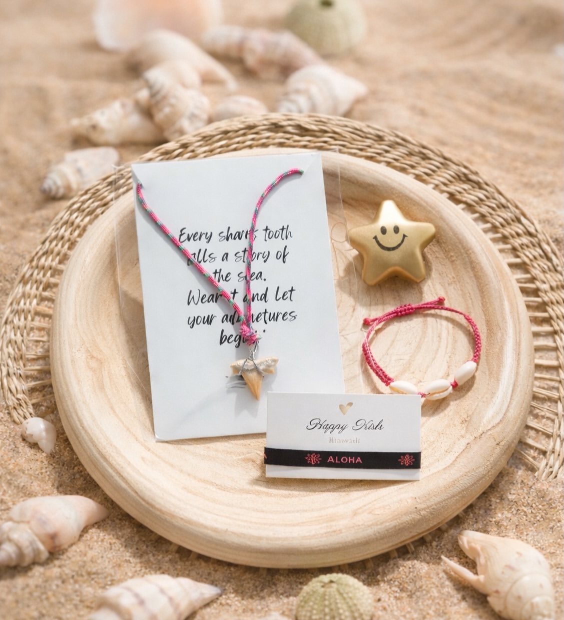 Beige wooden plate on sand with a white card, star pendant necklace, coral-pink cord, and a shell-themed bracelet for a beachy gift display.
